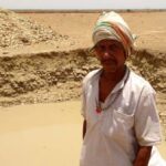 Pooran Adivasi near his farm pond with some water, even as the rest of the landscape wears a parched look. (Photo by Nachiket Sule)