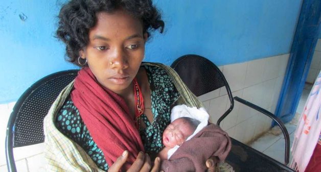 A young tribal woman waits with her newborn to receive the incentive given by the government to encourage institutional delivery (Photo by Rakhi Ghosh)