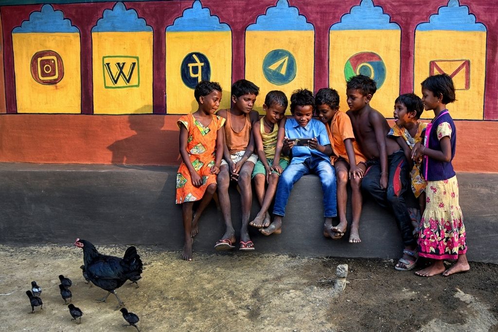 Children are seen watching a Cartoon movie on a Smartphone in front of a decorated wall with different Social Media symbol.