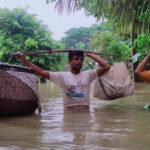 a couple going to a relief camp, wading through waist-deep water carrying the most valuable possessions